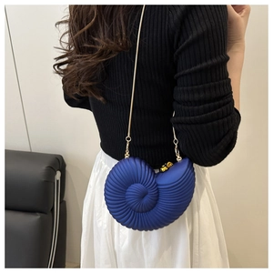 Detail of navy snail shell bag with matte texture and golden chain on a model