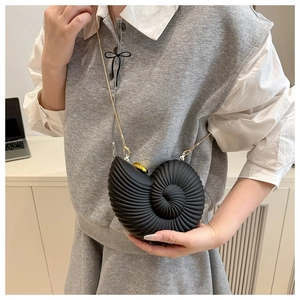 Detail view of the black conch-shaped crossbody bag with gold chain on model