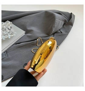 Detail of hand holding a high-gloss golden oval shell clutch with metal chain strap