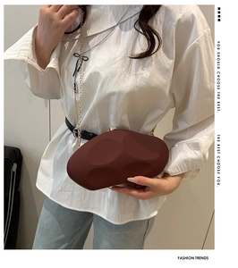 Deep red acrylic stone-shaped clutch bag with golden chain shown worn on a model