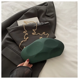 Detail of dark green acrylic clutch with geometric relief texture and gold metal chain