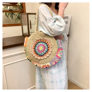 Détail du sac bohème rond en paille avec motif floral au crochet et une bandoulière chic
