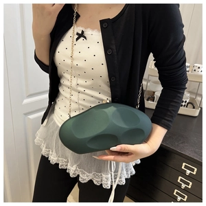 Detail of dark green acrylic evening bag with textured surface and gold chain strap