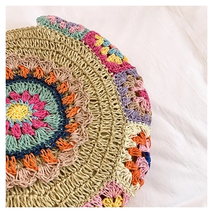 Détail du motif floral au crochet coloré sur un sac de plage rond en paille tressée