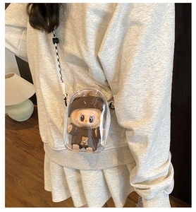 Detailed view of a transparent PVC doll display bag with a plush figure and woven strap