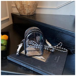 Detailed view of mini transparent PVC jelly bag with black trim and woven strap on a book