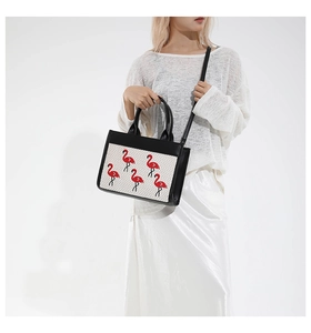 Détail du sac à main en cuir noir avec panneau tissé blanc et broderie flamant rouge