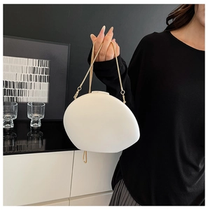 Minimalist white egg-shaped acrylic evening bag held by a model with a gold chain strap
