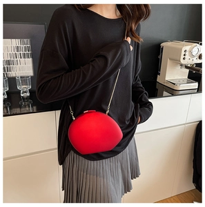 Detail view of a red pebble-shaped acrylic crossbody bag with a slim gold chain strap