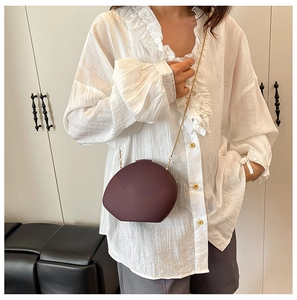 Macro shot of stylish burgundy shell bag with gold chain strap on white shirt