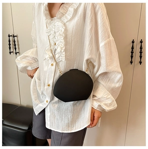 Detail of egg-shaped acrylic evening bag with gold chain strap on a white blouse