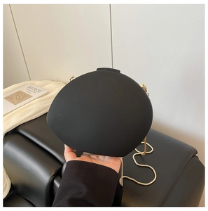 Detailed close-up of matte black egg-shaped evening clutch with gold chain and metal clasp