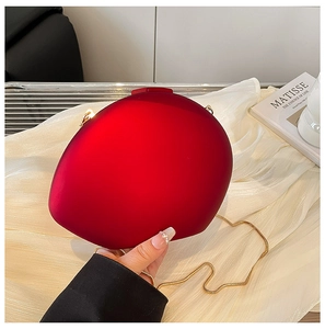 Close-up of heart-shaped matte red evening clutch bag with golden chain on white silk