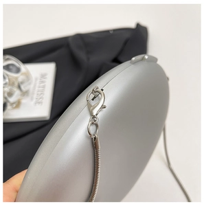 Close-up of silver oval hard shell evening bag featuring a metallic snake chain and lobster clasp