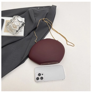 Detailed view of burgundy oval clutch bag with gold chain strap on a blazer fabric