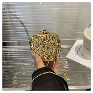 Detail of hand holding a gold sequin evening clutch bag with chain and spherical clasp