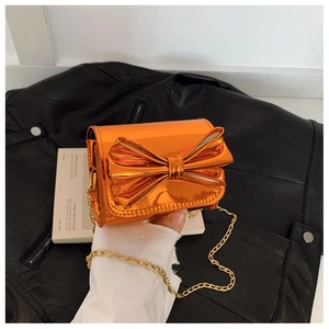 Détail d'un sac bandoulière en cuir verni orange avec un grand nœud et chaîne dorée