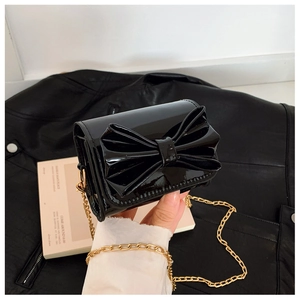 Détail du mini sac bandoulière en cuir verni noir avec nœud et fine chaîne dorée élégante
