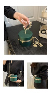 Detail of dark green cylindrical evening bag with gold bead handle and chain strap