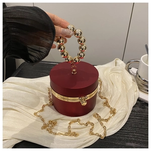 Macro detail of wine red acrylic cylinder clutch bag with golden bead handle and chain