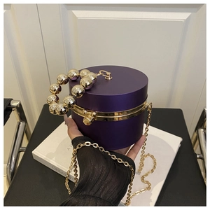 Detail of a purple cylindrical evening bag with gold beaded handle and metal chain strap