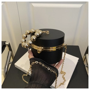 Detail of black cylindrical clutch bag with gold beaded handle and metal chain strap