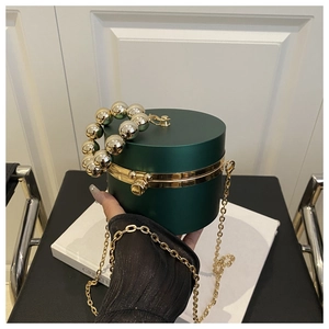 Detail of dark green cylindrical acrylic clutch with gold beaded handle and metal chain