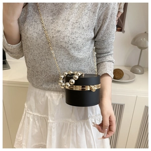 Close-up of black cylindrical acrylic evening bag with gold chain strap on female model