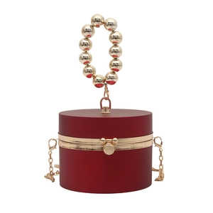 Detail of burgundy cylinder evening bag with gold sphere handle and chain strap