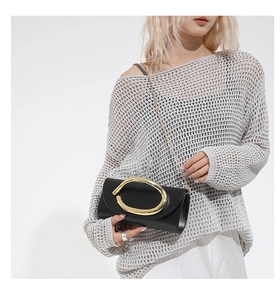 Dettaglio pochette in pelle nera con grande anello d'oro e sottile tracolla a catena