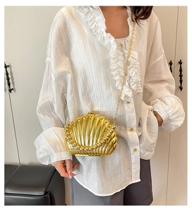 Golden seashell clutch with pearl details worn as a crossbody bag with a fine chain