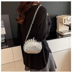 Silver shell-shaped clutch bag with sleek metal chain shown on model in modern setting