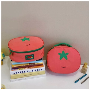 Detail of tomato-shaped nylon makeup bag with star-shaped leaves on stacked books