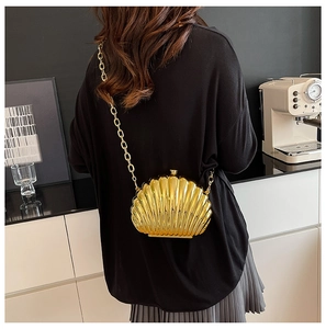 Chic gold shell-shaped acrylic clutch bag with metallic chain strap worn by a model