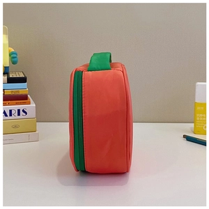 Detail view of the orange nylon makeup bag with green zipper and top handle
