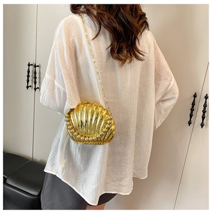 Detailed view of a golden shell-shaped evening bag with pearl trim and chain strap