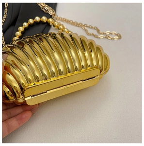 Detailed view of golden shell-shaped evening bag with pearl handle and metal texture