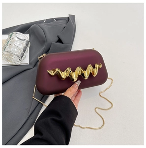Détail d'une pochette bordeaux mate avec ornement doré ondulé et fine chaîne serpent