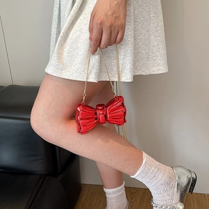 Glossy red bow-shaped mini lipstick bag with fine gold chain strap for shoulder wear