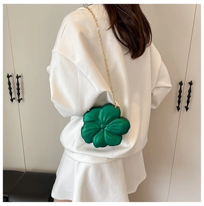 Close-up of green flower-shaped crossbody bag with gold chain strap worn by a model