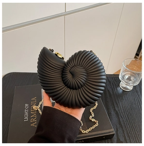 Dettaglio di pochette nera a forma di conchiglia con catena dorata su libri d'arte