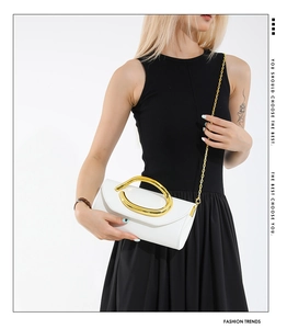 Detail of white leather clutch with sculptural gold handle and chain strap on model
