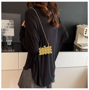 Detailed view of a gold studded mini crossbody bag with metallic chain on a model