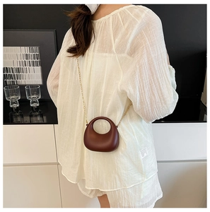 Détail du mini sac croissant marron foncé avec bandoulière chaîne dorée sur mannequin