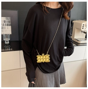 Detailed view of mini gold acrylic chain bag with spherical texture on a model