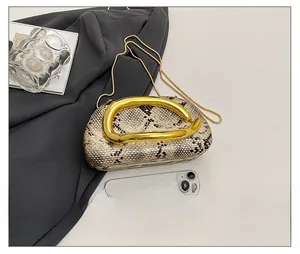 Détail de pochette en acrylique aspect serpent avec poignée en métal doré courbé