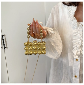 Detail of the acrylic evening clutch with gold metal sphere texture and pearl handle