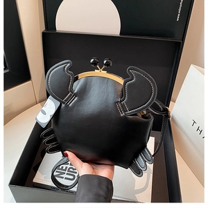 Detail of black crab-shaped crossbody bag with gold metal clasp and leather texture