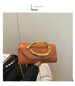 Detail of a brown fashion handbag featuring a large gold horseshoe buckle and chain