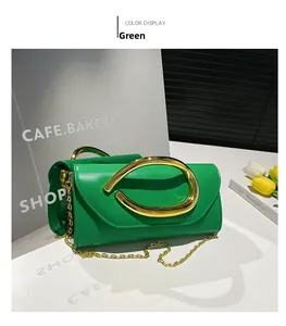 Close-up of green leather handbag with oversized gold metal handle and chain strap